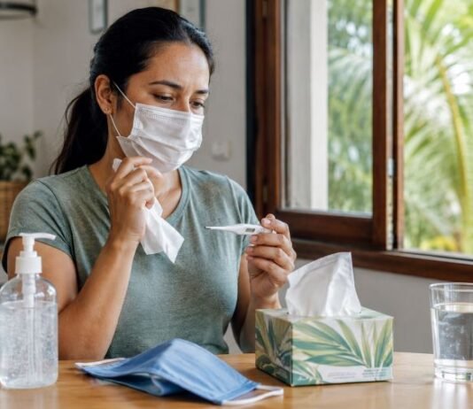 Rondônia fica fora do alerta atual, mas prevenção contra vírus respiratórios deve continuar Mulher de máscara verifica a temperatura em casa com álcool em gel e itens de prevenção sobre a mesa