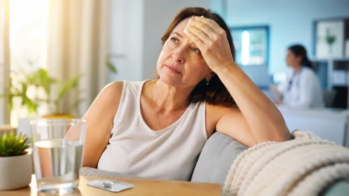Mulher com ondas de calor da menopausa segura compressa enquanto medicamento não hormonal aparece sobre a mesa