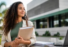 Concurso CRESS-RO tem inscrições prorrogadas até 30 de junho Candidata segura documentos ao lado de notebook em ambiente institucional, representando inscrições prorrogadas para o concurso CRESS-RO.