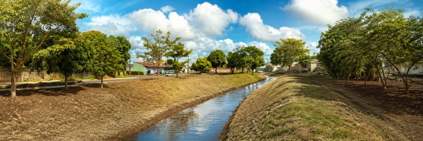 Vista panorâmica de igarapé limpo em Porto Velho, com canal desobstruído, margens organizadas, árvores e casas ao fundo.