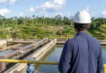 Edital pode redefinir água e esgoto em 40 municípios de Rondônia Trabalhador técnico observa estrutura de saneamento em Rondônia com tubulações e reservatório ao fundo