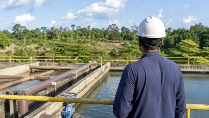 Trabalhador técnico observa estrutura de saneamento em Rondônia com tubulações e reservatório ao fundo