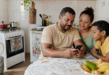 Famílias de Rondônia devem conferir vale do Gás do Povo de julho Família brasileira em cozinha simples consulta celular sobre o Gás do Povo em Rondônia