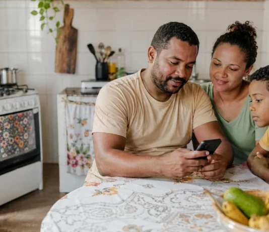 Famílias de Rondônia devem conferir vale do Gás do Povo de julho Família brasileira em cozinha simples consulta celular sobre o Gás do Povo em Rondônia