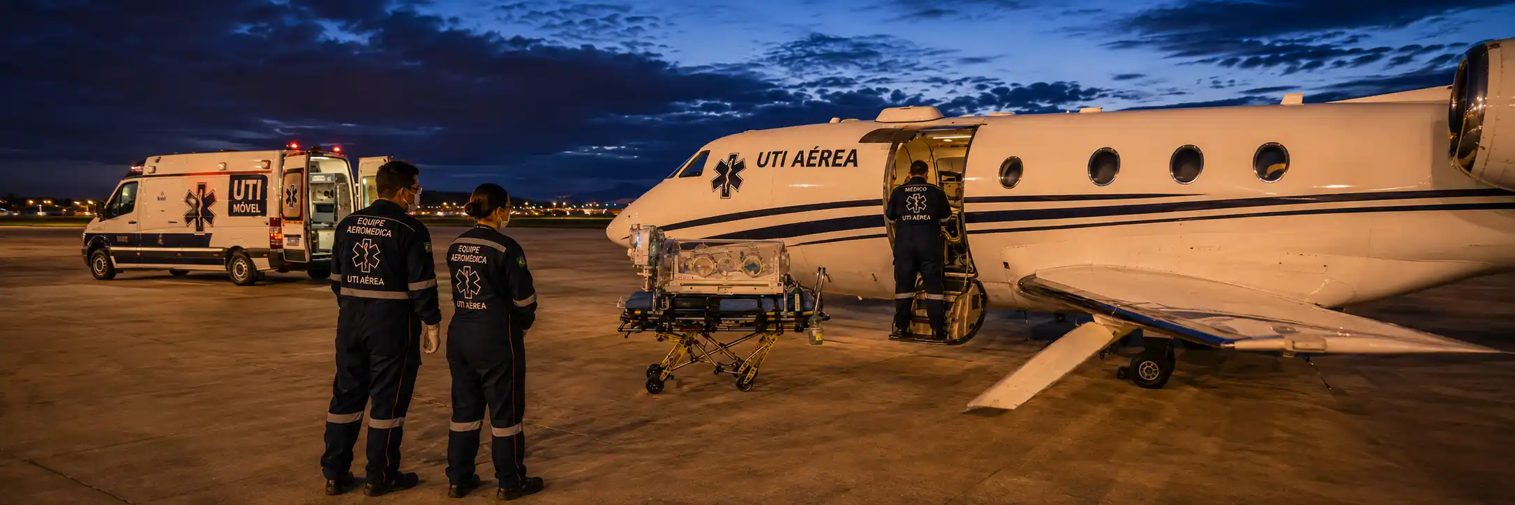 Equipe de UTI aérea organiza incubadora e equipamentos médicos próximos a aeronave e ambulância.