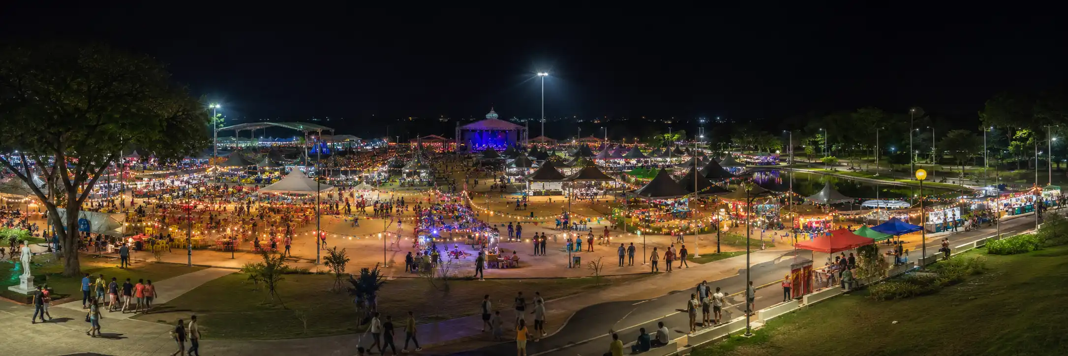 Vista panorâmica noturna de arraial representa o ambiente do Flor do Maracujá no Parque dos Tanques.