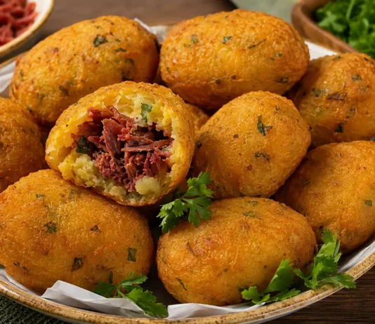 Bolinho de mandioca com carne-seca rende 50 unidades Bolinhos de mandioca dourados recheados com carne-seca, com uma unidade aberta mostrando o recheio