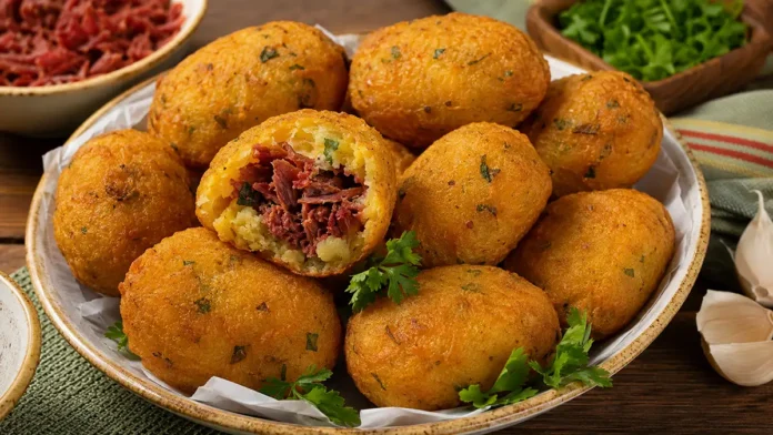 Bolinhos de mandioca dourados recheados com carne-seca, com uma unidade aberta mostrando o recheio