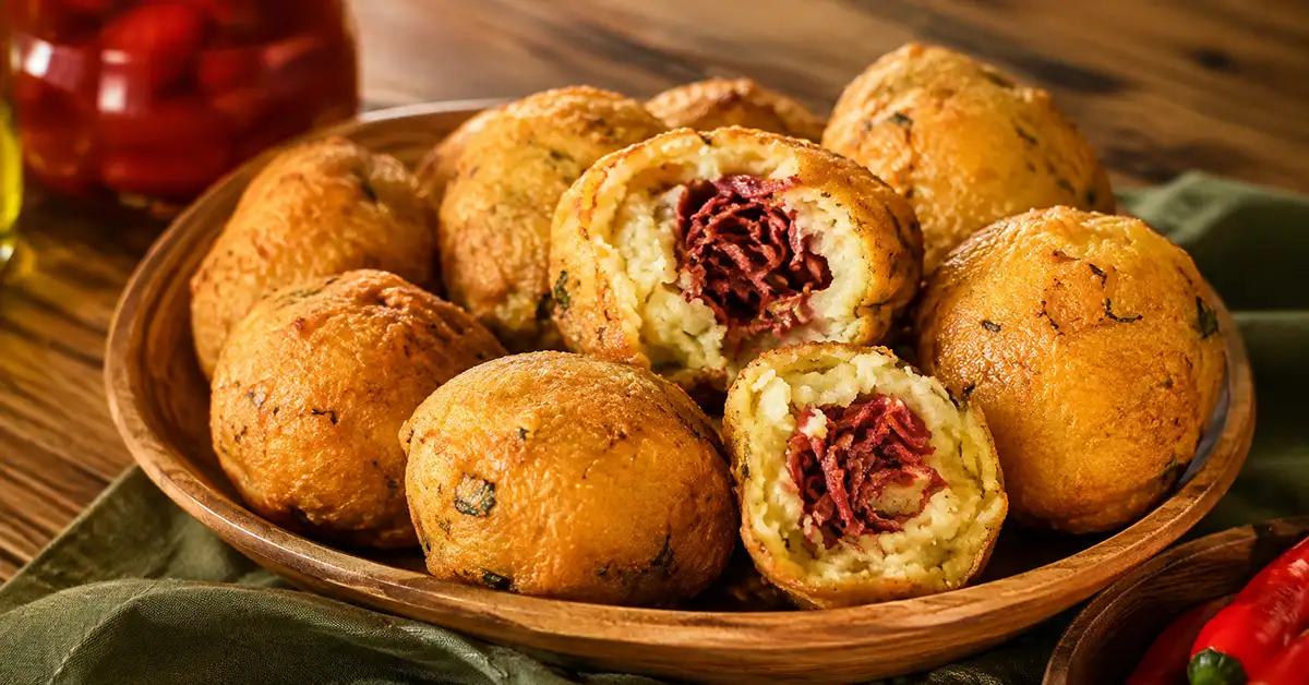 Bolinhos de mandioca fritos e dourados, com unidades abertas mostrando o recheio de carne-seca