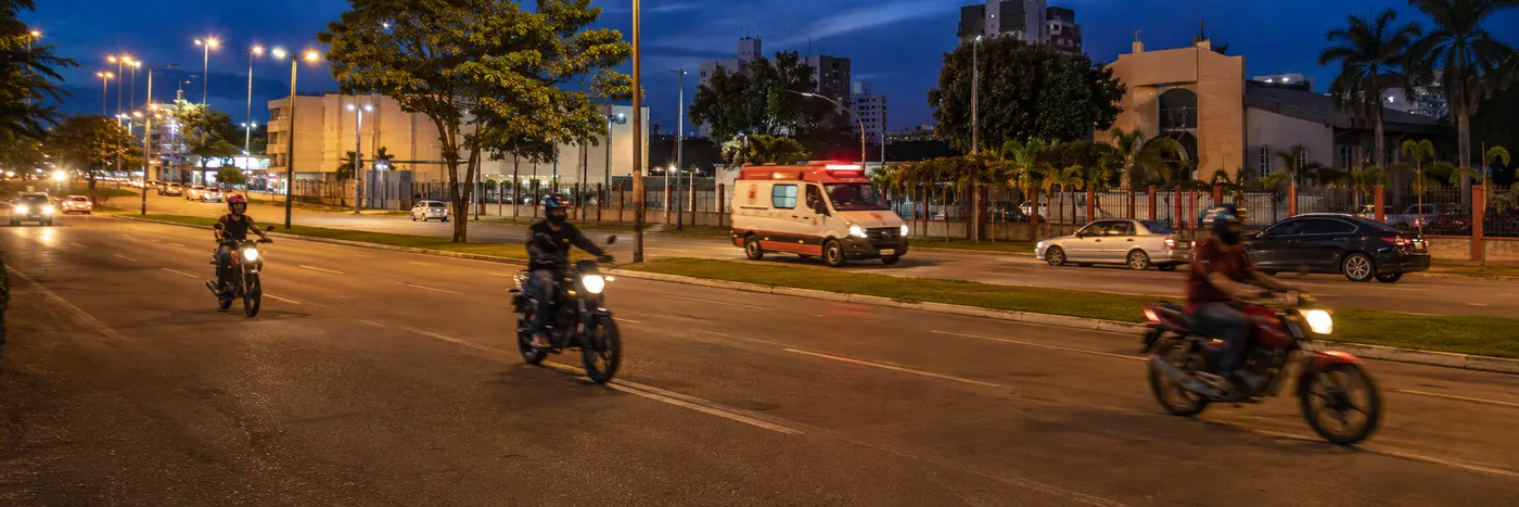 Motociclistas circulam à noite enquanto ambulância do SAMU passa por avenida de Porto Velho
