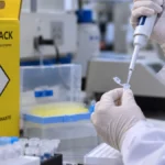 IFRO recebe sugestões até 2 de outubro para protocolo sobre acidentes com material biológico Consulta pública do IFRO: ilustração de mãos com luvas manipulando amostra em bancada laboratorial e coletor de perfurocortantes