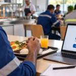 Empresas e nutricionistas do PAT têm até 9 de novembro para refazer cadastro Trabalhador em refeitório empresarial com refeição e notebook representando o recadastro do PAT