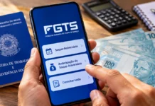 Antecipação do FGTS terá limite de três parcelas a partir de novembro Celular com referência ao saque-aniversário do FGTS ao lado de carteira de trabalho e cédulas de real