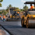 Novo Horizonte do Oeste tem 1,3 km de ruas asfaltadas e outros 1,2 km em preparação Asfalto em Novo Horizonte do Oeste ilustrado por obra urbana com trabalhadores e compactadora.