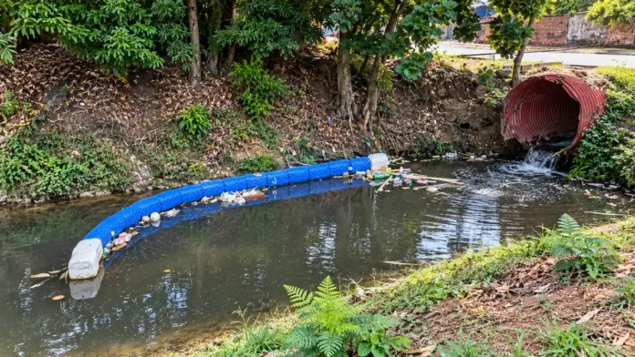 Ecobarreira do Belmont em composição editorial baseada em fotos de referência, mostrando barreira flutuante azul e resíduos retidos no igarapé.