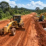 RO-494 recebe terraplanagem e drenagem em 1,5 km RO-494 em Primavera: ilustração de motoniveladora e retroescavadeira trabalhando em estrada de terra com manilhas de drenagem.