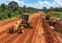 RO-494 recebe terraplanagem e drenagem em 1,5 km RO-494 em Primavera: ilustração de motoniveladora e retroescavadeira trabalhando em estrada de terra com manilhas de drenagem.